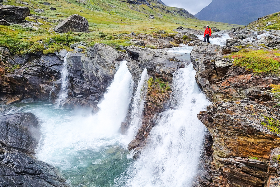 Ensam vandrare poserar framför ett vattenfall i Ladtjovagge