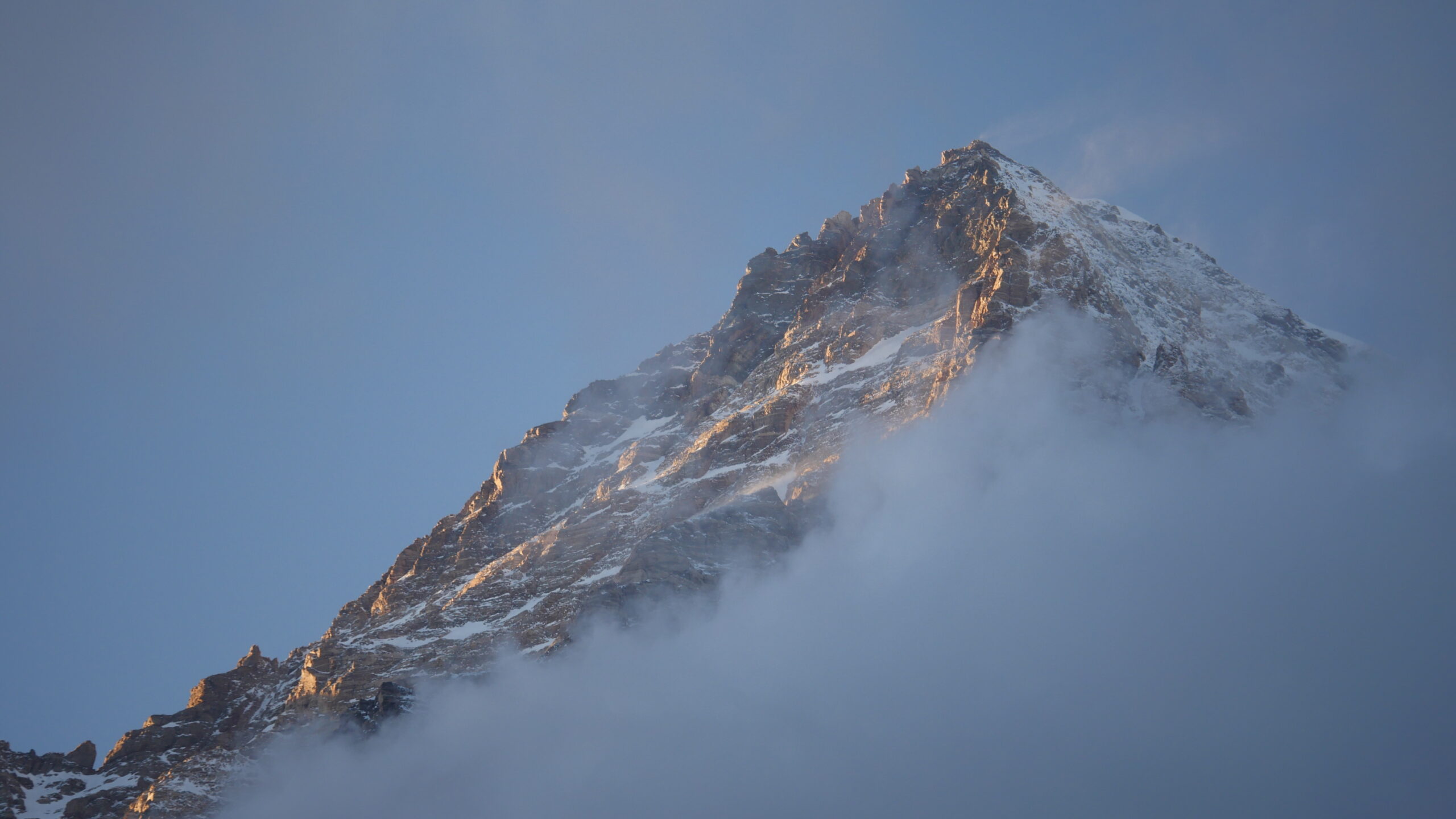 Toppen av K2 i Pakistan under solnedgång uppslukad bland moln
